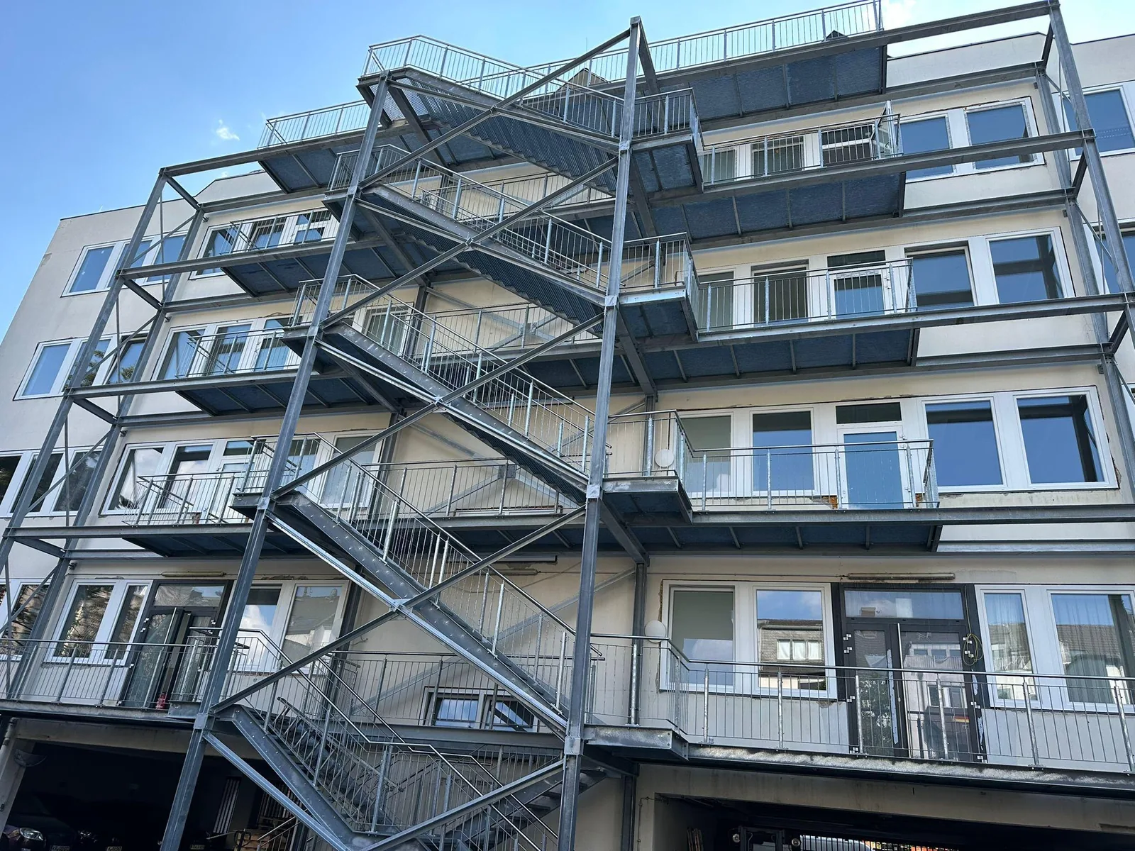 Verzinkte Außentreppenanlage mit Podesten und Geländern an einer mehrgeschossigen Fassade.